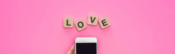 在立方体附近拿着智能手机的女人的局部视图 带有粉红背景的爱的字母 全景镜头 — 图库照片