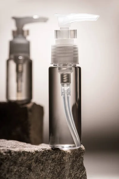 バックライト付きの暗い背景の石の上のディスペンサー化粧品ボトルの選択的な焦点 — ストック写真
