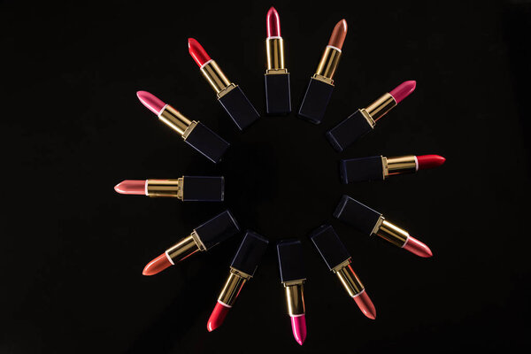 top view of assorted lipsticks in luxury tubes arranged in circle isolated on black