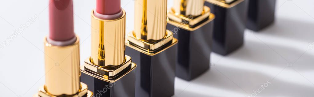 close up view of assorted lipsticks in luxury tubes in line on white background, panoramic shot