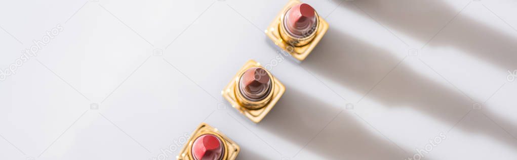 top view of assorted lipsticks in luxury tubes in line on white background, panoramic shot