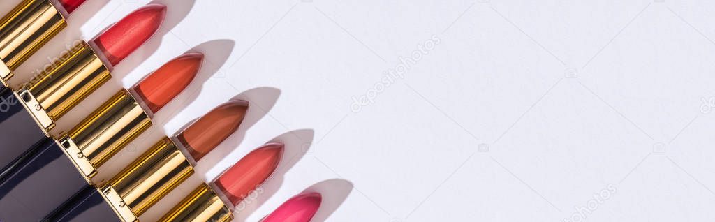 top view of assorted lipsticks in luxury tubes in line on white background, panoramic shot