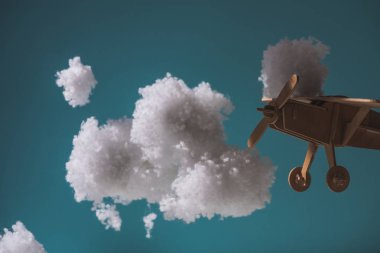 Beyaz tüylü bulutların arasında uçan tahta oyuncak uçak. Koyu renkli pamuktan yapılmış.