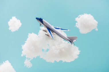 Beyaz pamuklu bulutların arasında uçan oyuncak uçak mavi üzerinde izole edilmiş pamuk yününden
