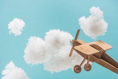 Beyaz tüylü bulutların arasında uçan ahşap oyuncak uçak mavi üzerinde yünlü pamuktan yapılmış.