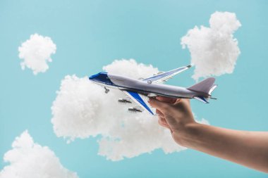 Beyaz pamuklu bulutların arasında oyuncak uçakla oynayan bir kadının mavi yününden yapılmış görüntüsü.