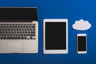 Dizüstü bilgisayar, akıllı telefon ve dijital tablet yakınlarındaki boş beyaz kağıt bulutunun üst görünümü mavi ekranda izole edilmiş