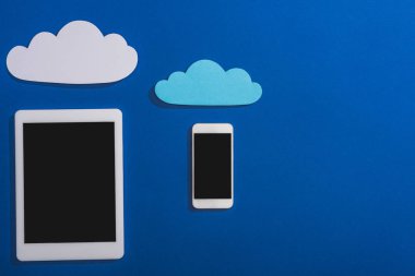 Akıllı telefon ve dijital tablet yakınlarındaki boş kağıt bulutların mavi üzerine izole edilmiş boş ekran görüntüsü