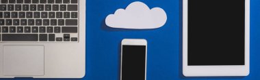 Dizüstü bilgisayar, akıllı telefon ve dijital tablet yakınlarındaki boş beyaz kağıt bulutu üst görünümü mavi, panoramik çekim izole