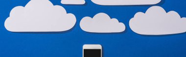 top view of white paper cut clouds and smartphone on blue background, panoramic shot clipart