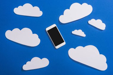 Beyaz kağıdın üst görünümü mavi arkaplanda bulutları ve akıllı telefonu keser