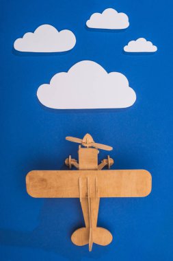 top view of wooden toy plane in blue sky with paper cut white clouds clipart