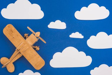 Mavi gökyüzünde beyaz bulutları kesen tahta oyuncak uçak manzarası.