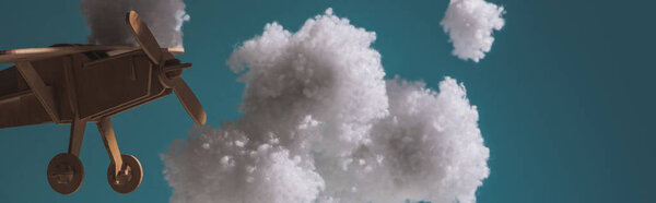 wooden toy plane flying among white fluffy clouds made of cotton wool in dark, panoramic shot