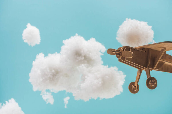 wooden toy plane flying among white fluffy clouds made of cotton wool isolated on blue