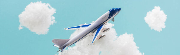 toy plane flying among white fluffy clouds made of cotton wool isolated on blue, panoramic shot