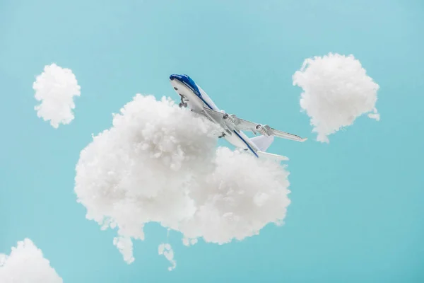 青い上に隔離された綿ウールで作られた白いふわふわの雲の間を飛ぶおもちゃの飛行機 — ストック写真
