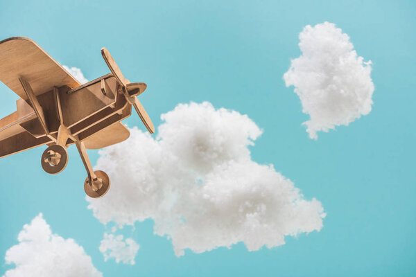 wooden toy plane flying among white fluffy clouds made of cotton wool isolated on blue