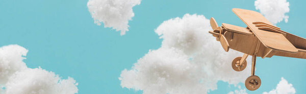 wooden toy plane flying among white fluffy clouds made of cotton wool isolated on blue, panoramic shot