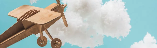 wooden toy plane flying among white fluffy clouds made of cotton wool isolated on blue, panoramic shot