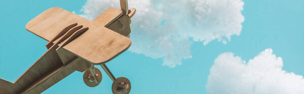 wooden toy plane flying among white fluffy clouds made of cotton wool isolated on blue, panoramic shot