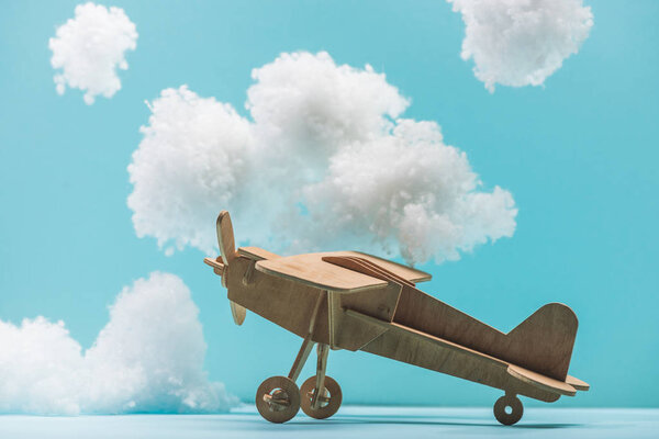 деревянная игрушечная плоскость среди белых пушистых облаков из ваты, изолированных на голубом

