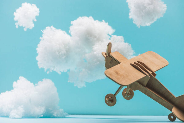 деревянный игрушечный самолет, летающий среди белых пушистых облаков из ваты, изолированных на голубом
