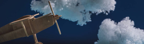 деревянный игрушечный самолет, летящий среди белых пушистых облаков из ваты, изолированных на темно-синем, панорамном снимке
