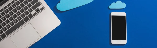 笔记本电脑附近空白纸云的顶部视图 带有空白屏幕的智能手机 蓝色全景截图 — 图库照片
