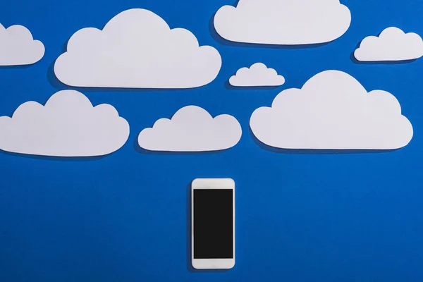 top view of white paper cut clouds and smartphone on blue background