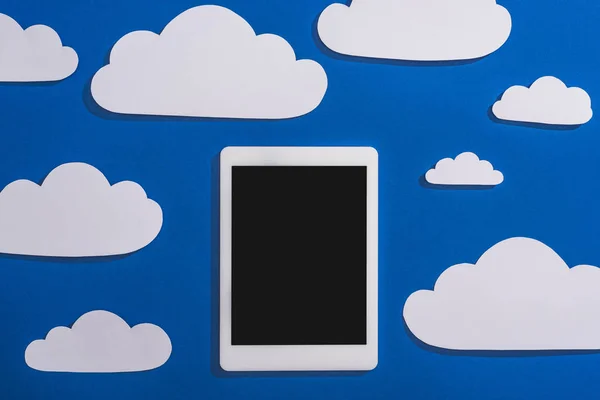 top view of white paper cut clouds and digital tablet on blue background