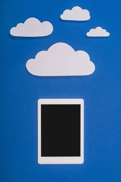 top view of white paper cut clouds and digital tablet on blue background