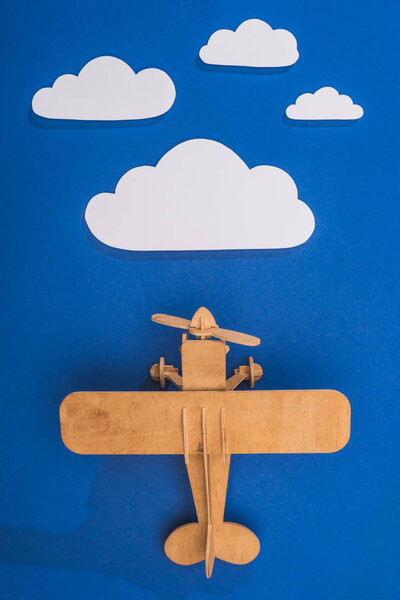 top view of wooden toy plane in blue sky with paper cut white clouds