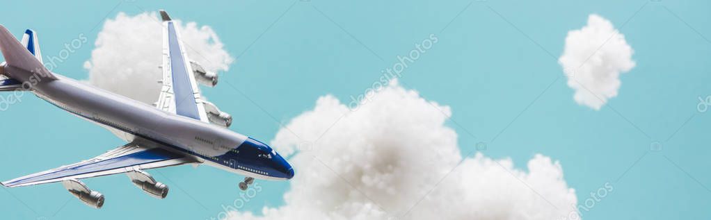 toy plane flying among white fluffy clouds made of cotton wool isolated on blue, panoramic shot