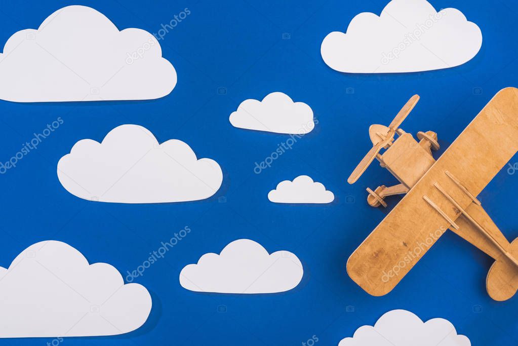 top view of wooden toy plane in blue sky with paper cut white clouds