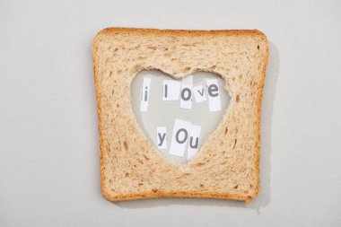 Top view of bread slice with carved heart shape and i love you lettering on grey background clipart