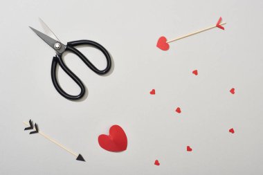 Gri arkaplanda oklar, makas ve kağıt kalplerin üst görünümü