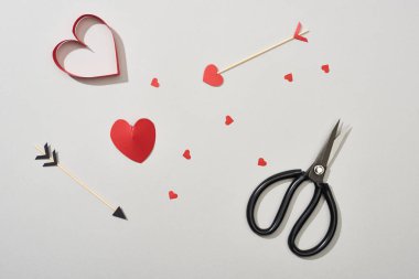 Top view of heart shaped papers with arrows and scissors on grey background clipart