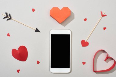 Boş ekranlı akıllı telefonun üst görünümü ve gri arkaplanda okları olan kalp şekilli kağıtlar
