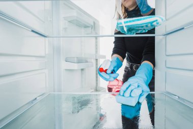 Cropped view of woman in rubber gloves cleaning refrigerator with detergent isolated on white clipart