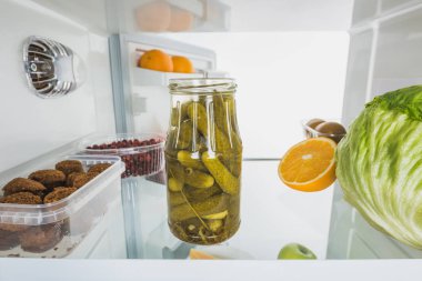Jar of pickles with cabbage, fruits and cutlets in refrigerator with open door isolated on white clipart