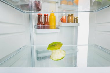 Selective focus of bitten apple with sauces on open fridge door isolated on white clipart