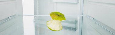 Panoramic shot of gnawed green apple in refrigerator with open door isolated on white clipart