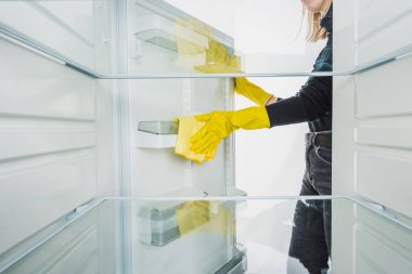 Lastik eldivenli bir kadının beyaz buzdolabını temizlerken çekilmiş görüntüsü.