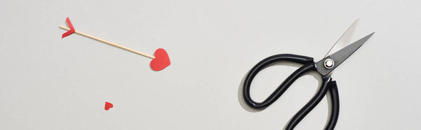 Top view of scissors and arrow with heart shape on grey background, panoramic shot