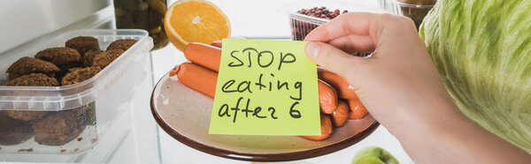 Cropped view of food in fridge and woman holding card with stop eating after six lettering isolated on white, panoramic shot