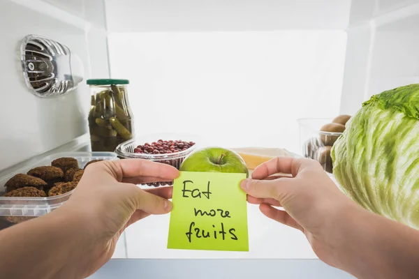 Cropped view of woman holding card with eat more fruits lettering with food in fridge at background, isolated on white — Stock Image Cropped View Woman Holding Card Eat More Fruits Lettering Food Royalty Free Stock Photos