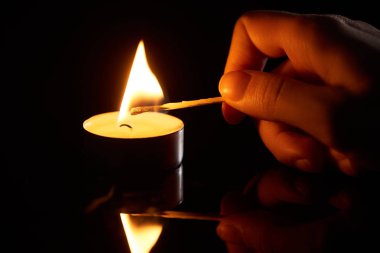 selective focus of woman lighting up candle with match isolated on black clipart