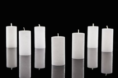 selective focus of white candles with reflection isolated on black clipart