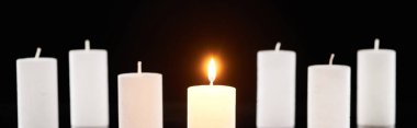 selective focus of burning white candles glowing near another isolated on black, panoramic shot clipart